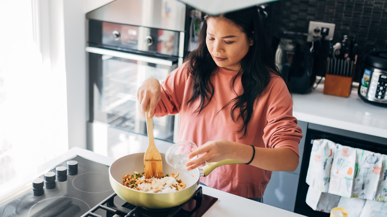 woman making fried rice on stove in lighted kitchen