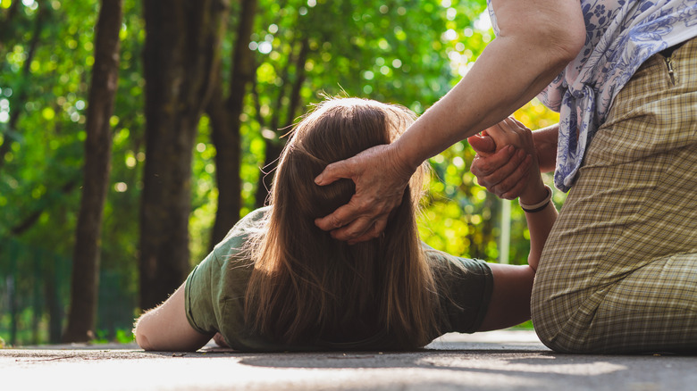 unconscious teenager receiving help from woman