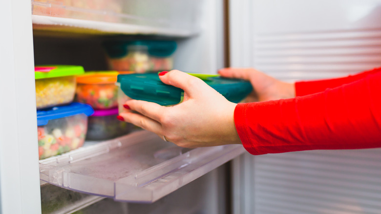 Pair of hands placing a plastic container of leftovers into the fridge