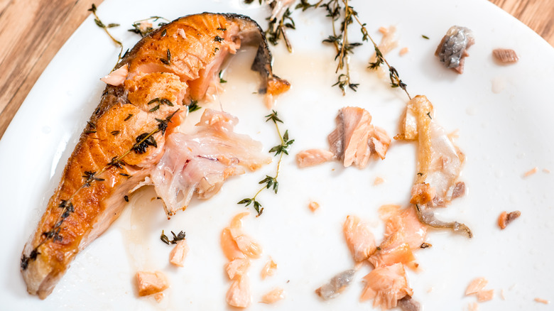 Half eaten salmon filet on white plate on top of a wooden table