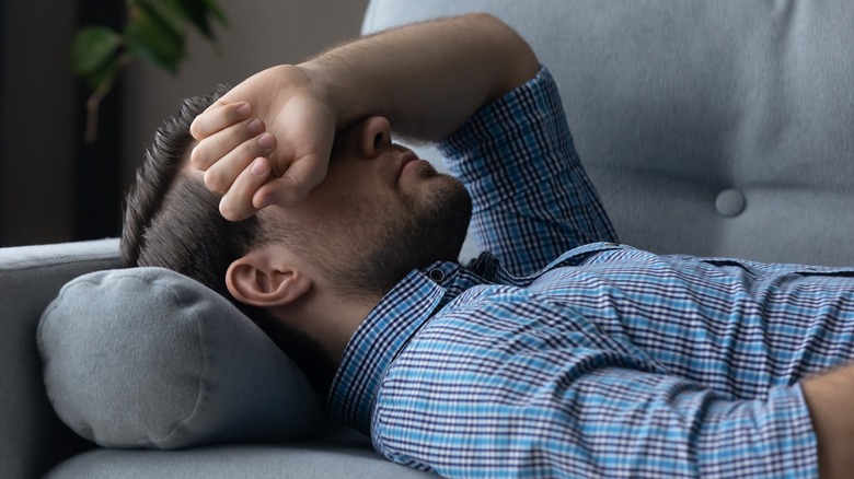Man laying on couch covering eyes