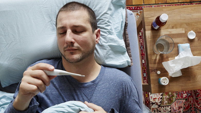 man sick in bed looking at thermometer