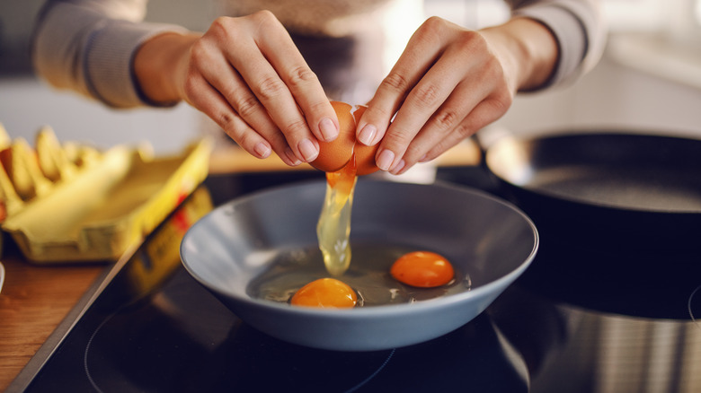 woman's hands breaking eggs into a frying pan