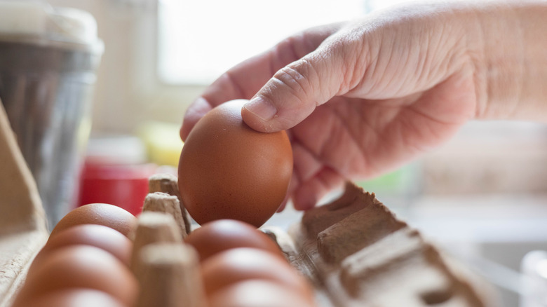 man's hand pulling brown eggs from carton