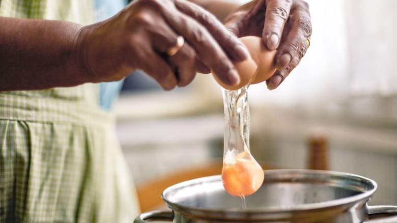 woman's hands cracking egg into saucepan