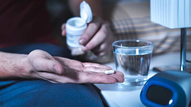 A man's hand holding a pill and a pill bottle next to a glass of water