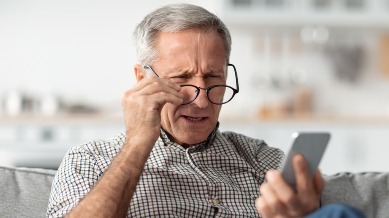 older man squinting while looking at his phone