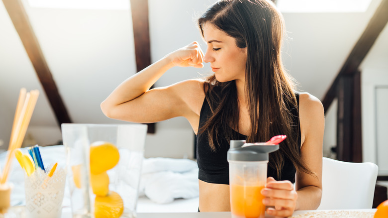 woman flexing her bicep while making a protein shake