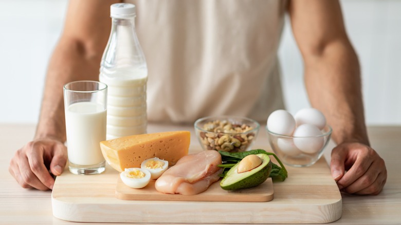 man standing in front of cheese, milk, eggs, and nuts on a cutting board