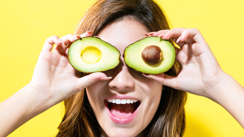 Woman covering her eyes with two avocado halves