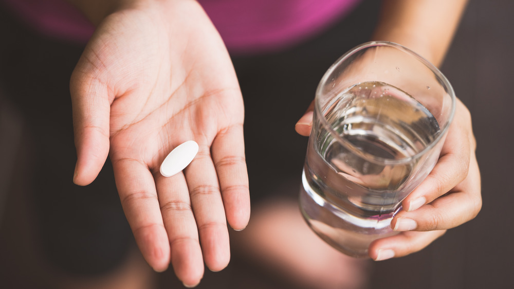 Closeup of two hands, one holding a large white pill and one holding a glass of water