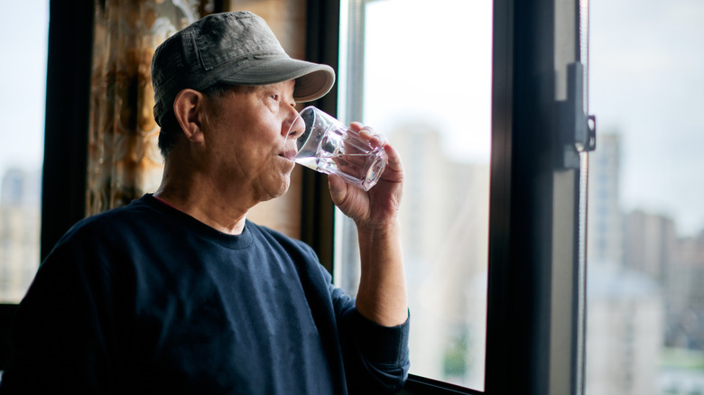 Man looking out window drinking glass of water