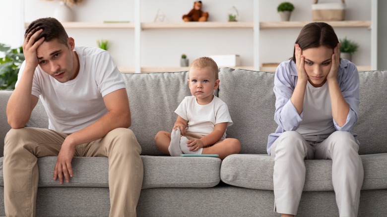 baby sitting between frowning mom and dad