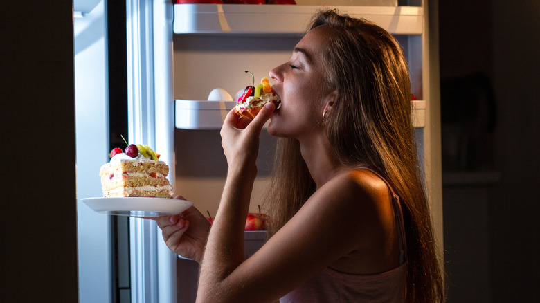 woman eating cake from fridge at night