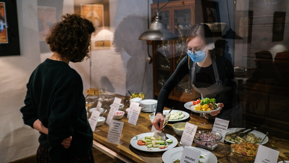 A waitress wears a protective face mask as she prepares a breakfast dish for a client behind a protective plastic shield inside Kolanko No 6 Restaurant in Krakow, Poland.