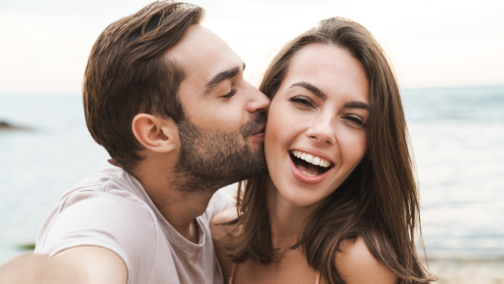 young man taking a selfie of kissing a woman on the cheek 