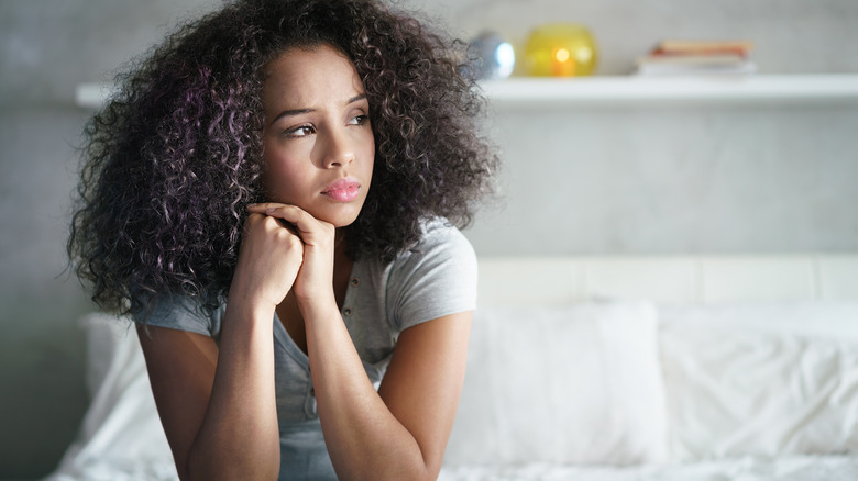 Young woman sitting on bed looking lonely