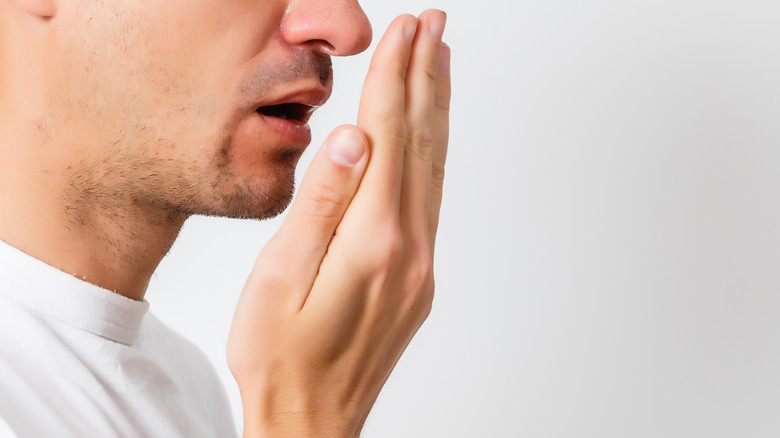 close up of a man checking for bad breath by breathing into his hand