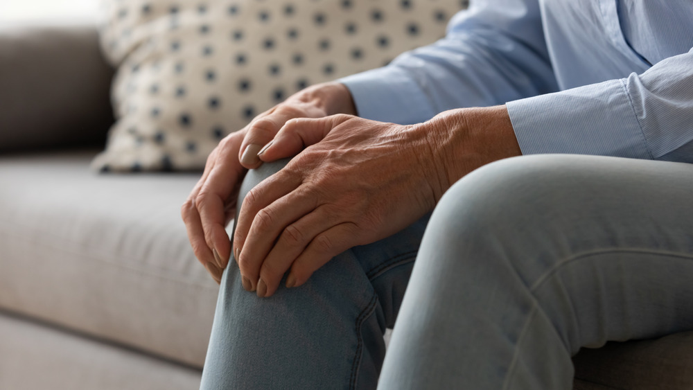 Woman sitting on couch holding painful knee