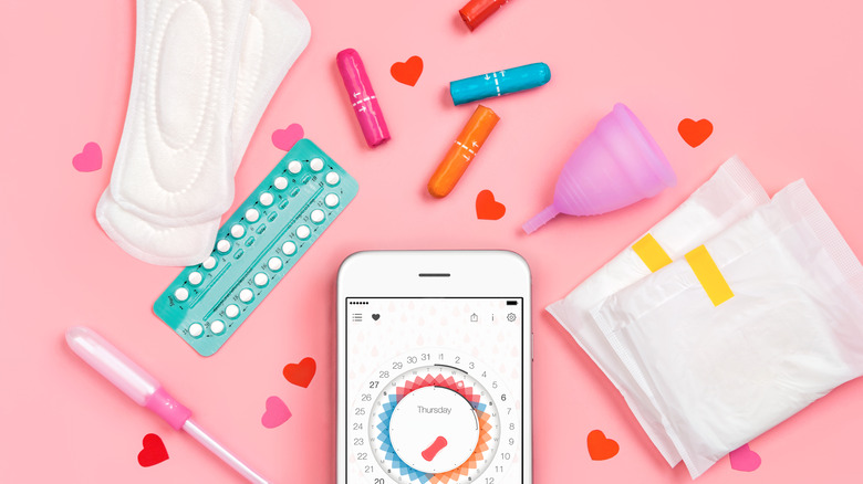 Sanitary napkins, tampons, contraceptive pills and menstrual cup on pink background