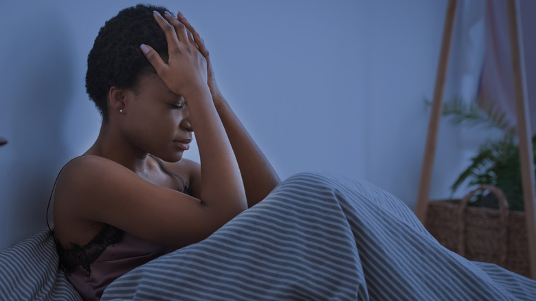 Woman sitting up in bed with head in her hands