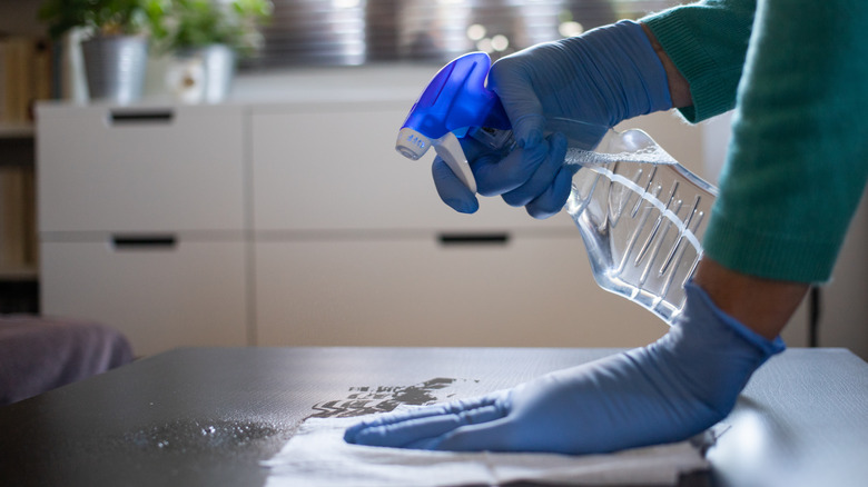 Gloved hands spraying cleaning solution on table in their home