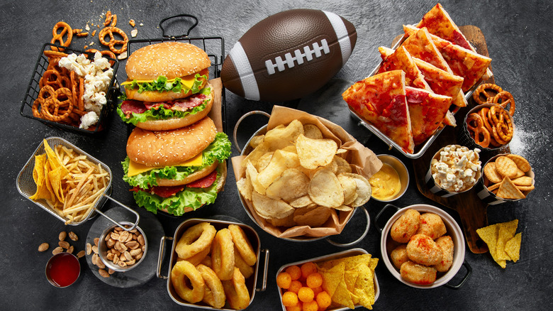 A football surrounded by hamburgers, chips, onion rings, and other snack foods