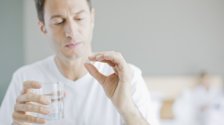 man holding pill and glass of water