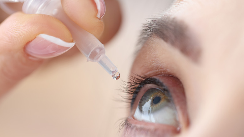 person putting eye drops into eye