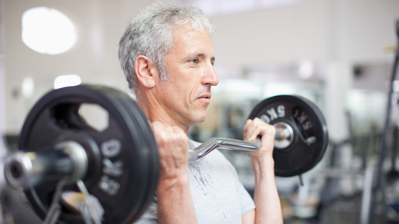 older man standing with a barbell across his chest