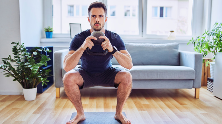 man performing a goblet squat on a mat at home