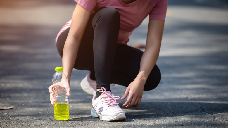 Woman tying shoes holding electrolyte drink