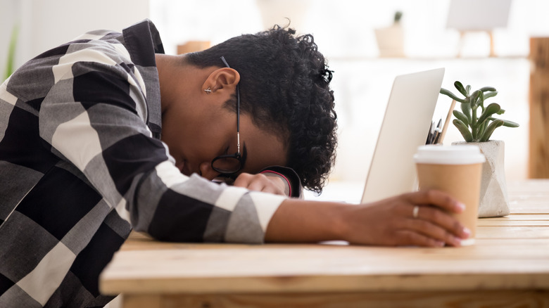 Person face down on desk holding coffee