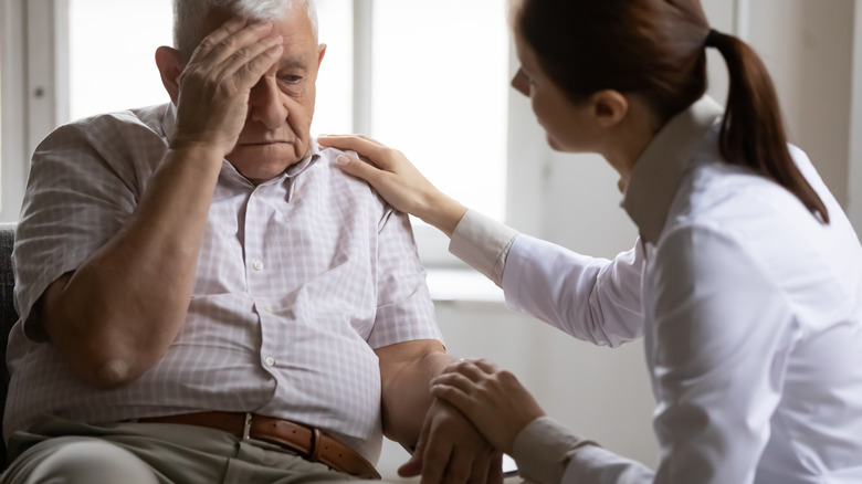 an elderly man holding his head, talking about migraines with a doctor