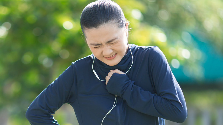 Woman running outside puts her hand to her chest and grimaces