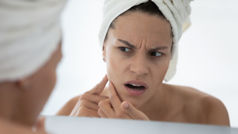 woman examines face in mirror