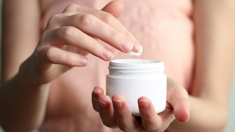 Fingers dipping into lotion container
