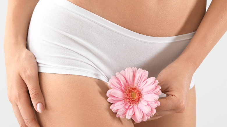 Woman holding a pink flower in front of her private parts