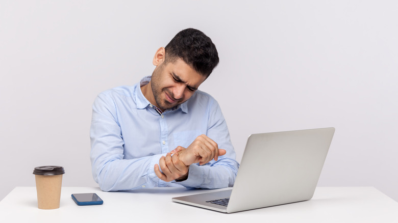 Man at desk with laptop holding his wrist and wincing