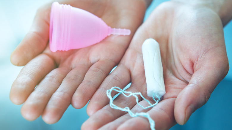 Hands holding a tampon and menstrual cup