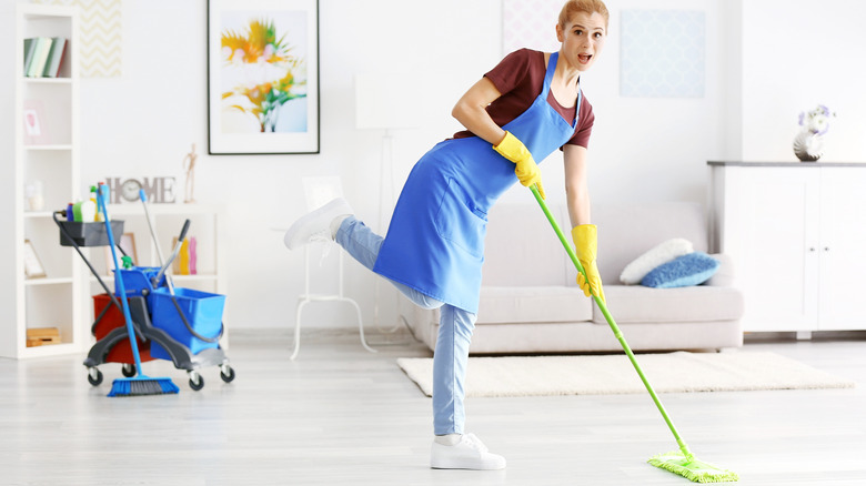 Funny young woman mopping living room floor