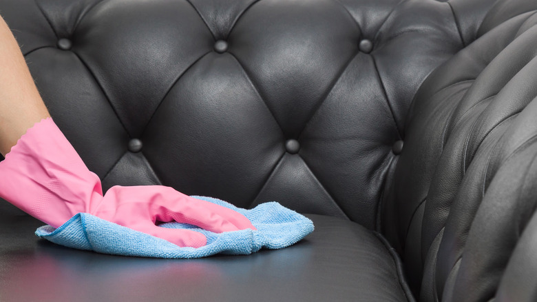 Pink gloved hand wiping down leather couch