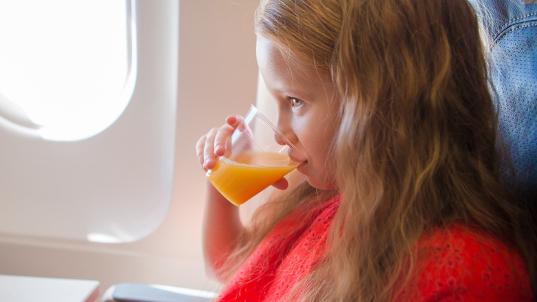 Young girl drinking orange juice while seated on plane