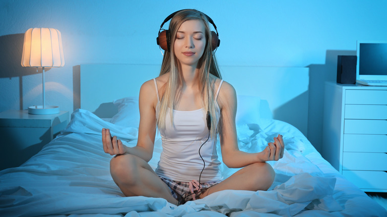 woman meditating with headphones on bed