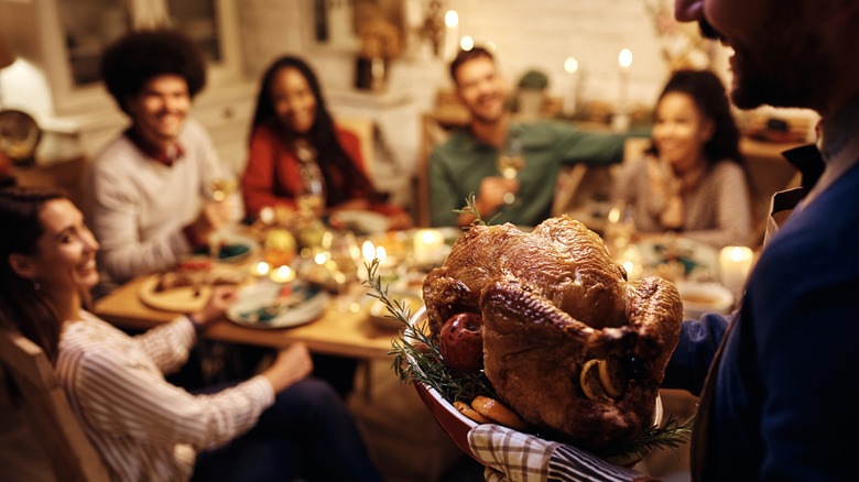 woman bringing cooked turkey to table of people