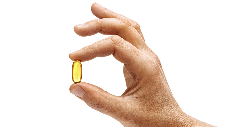 Hand holding a yellow supplement capsule on white background