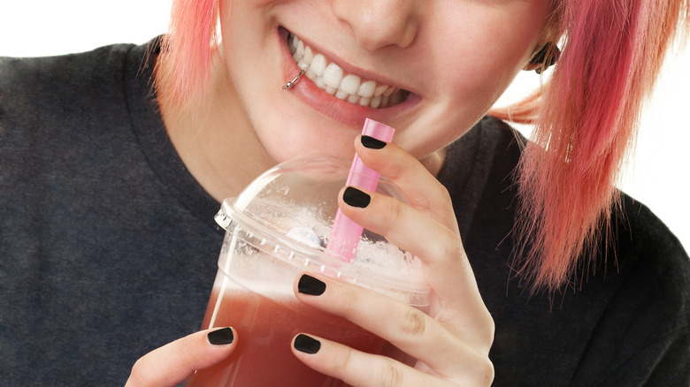 Smiling woman with lip piercing holding to-go beverage