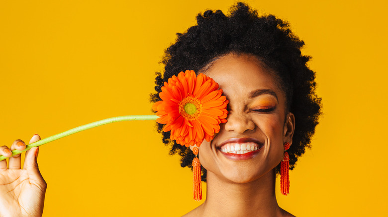 woman smiling big with a flower over one eye