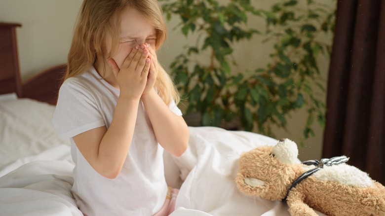 girl sneezing because of dust mite allergy on bed