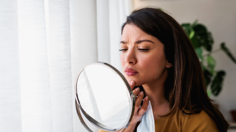 Woman looking in mirror with a concerned look, touching her lip
